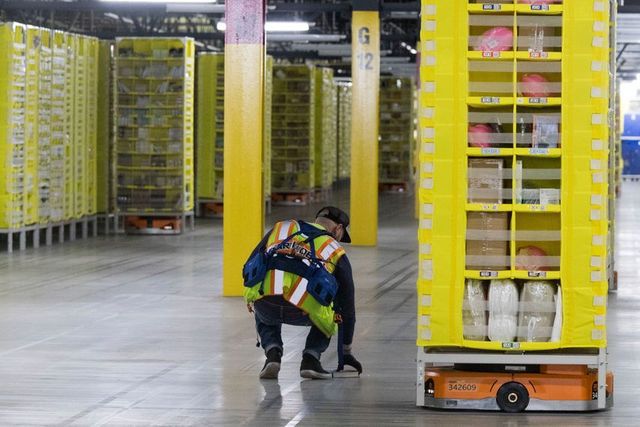 An Amazon worker retrieves a book that fell off a pod at the Amazon fulfillment center on Staten Island